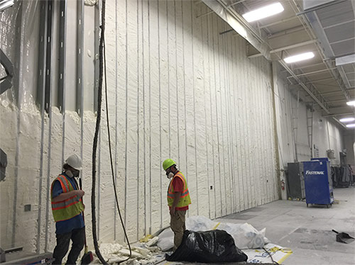 Workers in a large commercial space filling the walls with insulating foam