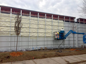 Worker in a construction lift filling a large exterior wall with insulating foam