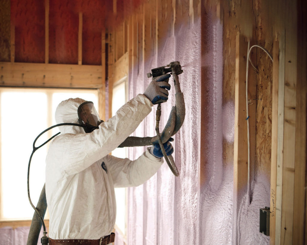 Man in protective suit spraying a wall with insulating material